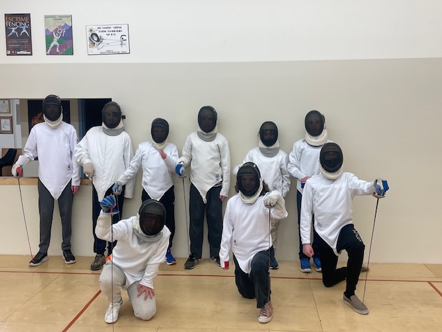 A group of beginner fencers in masks and jackets lined up in the club