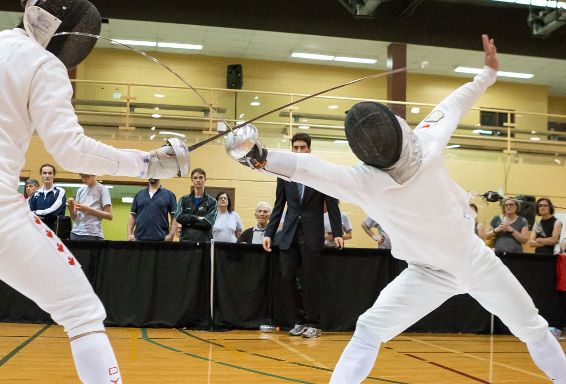 Two fencers bouting in the Damocles gym while spectators watch